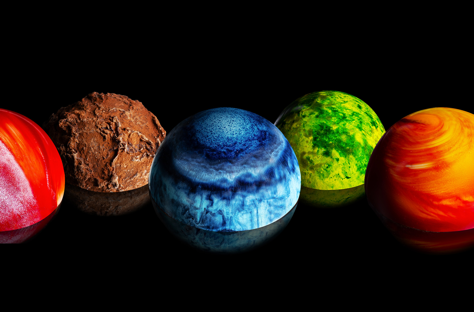 Cinq ganaches de David Chocolatier, colorées comme des planètes, sur fond noir